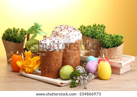 Beautiful Easter cakes, colorful eggs and candles on wooden table on yellow background