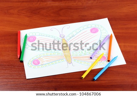 Children's drawing of butterfly and pencils on wooden background