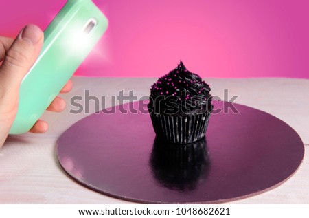Food blogging, desserts blog concept. Closeup of hand with smartphone taking picture of cupcake 
