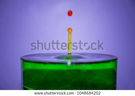 a moment captured when a red droplet falls onto a green solution and bounces back