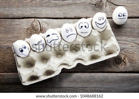 Eggs with funny faces in carton package on wooden table