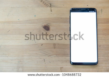 Top view mock up image of a black mobile phone with white screen on a wooden surface.