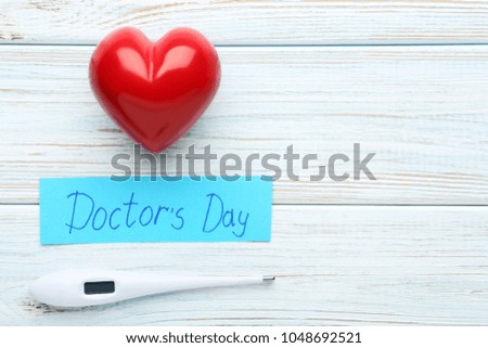 Inscription Doctors Day with thermometer and red heart on wooden table