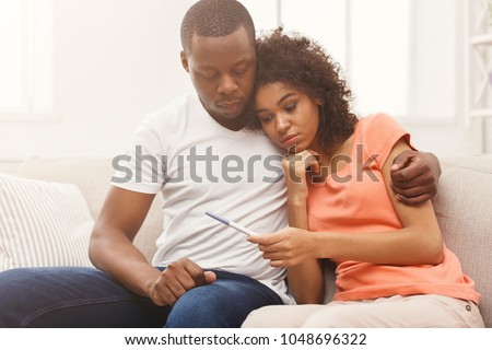 Sad african-american couple after negative pregnancy test result, sitting on couch at home, copy space Royalty-Free Stock Photo #1048696322