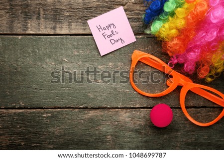 Inscription Happy Fools Day with glasses and wig on wooden table