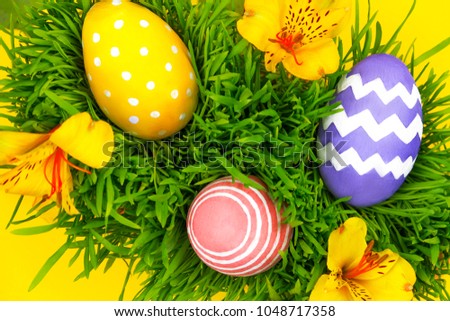 Happy Easter Day. Colorful tradition easter eggs lying on green grass with spring's flowers on yellow background