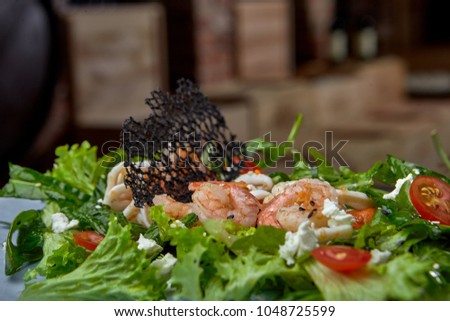 Salad with shrimps cheese, arugula, cherry tomatoes and lettuce leaves. On a platter of manual production. on a wooden stand.