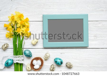 blank photo frame with easter eggs and spring flowers mock up over white wooden table. top view. flat lay