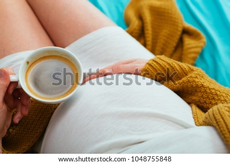 Pregnant woman drinking coffee. Aerial close up view. Royalty-Free Stock Photo #1048755848