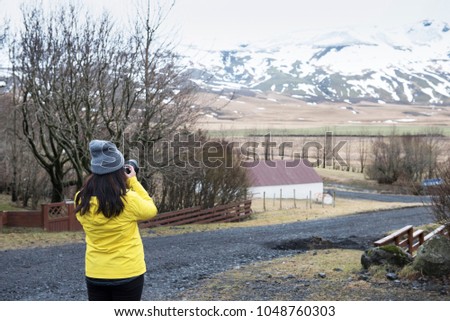Long hair young asian lady in yellow warm shirt use camera capture photo of Icelandic snowcapped  mountain view in winter. 
