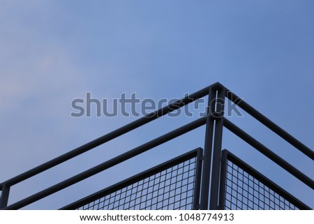 Close up outdoor view from bellow of a metallic barrier with the blue sky in background. Pattern of dark parallel lines and angles. Abstract architectural image. Geometric design. Iron elements.    