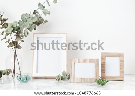 Three frames mockup, front view, with decor elements, flowers and blank copy space over the white wall.