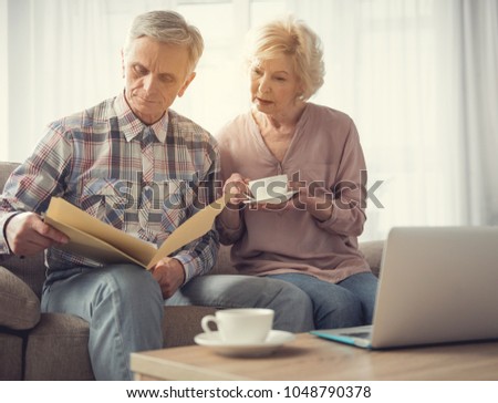 Calm mature man and woman sitting in living room and looking at folder with papers Royalty-Free Stock Photo #1048790378