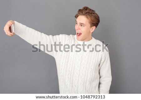 Young man wearing sweater studio isolated on grey taking selfie photos joyful
