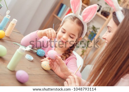 Mother and daughter in bunny ears easter celebration together at home sitting girl making dots with brush joyful