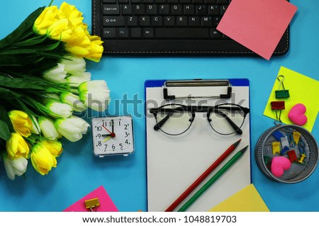 office workspace. Clock. artificial flowers, stationery, glasses, keyboard. toned background
