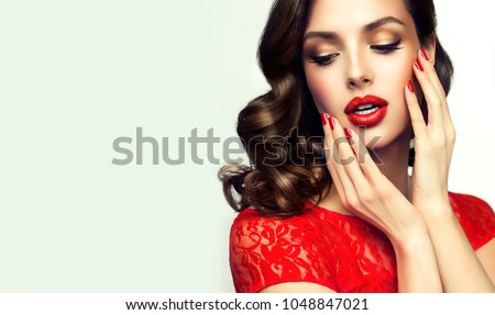 Beautiful    model  girl  with curly brown  hair . Brunette woman with wavy hairstyle  . Red  lips ,dress and  nails manicure .    Fashion , beauty and make up portrait