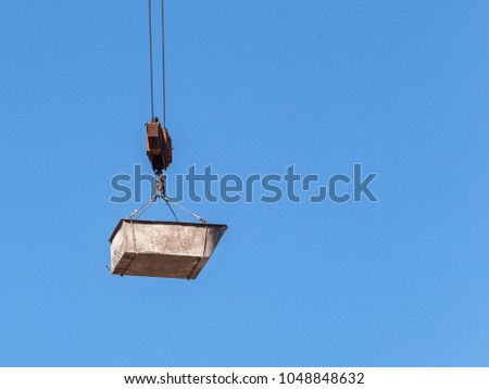 Hook block of tower crane with a bucket on ropes at a blue sky background