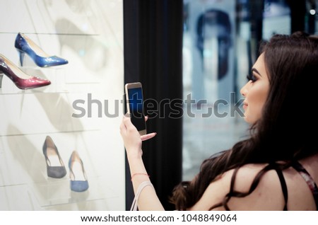 Girl or a woman in a shopping mall photographs shoes from the shop window