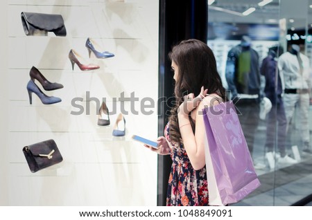 Girl or a woman in a shopping mall photographs shoes from the shop window