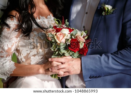 beautiful young bride with long dark hair and a long white wedding dress holding a bridal bouquet of bright red roses