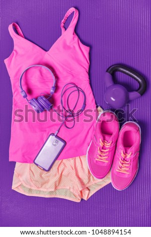Activewear fitness clothes outfit - cute pink fashion matching clothing for girl training with weights and phone headphones to listen to music during workout at gym on purple exercise mat background.