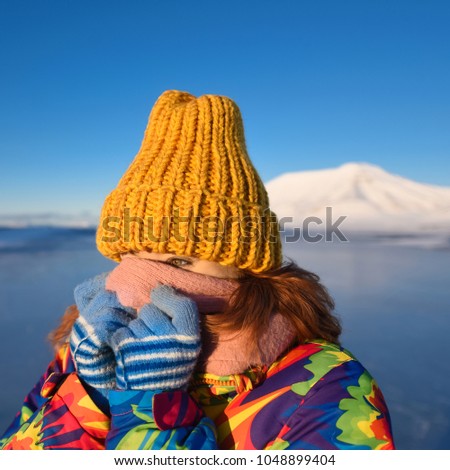 Close-up of a girl in a rainbow down jacket yellow knitted cap with red hair beautiful young hair  on the background of the mountain Svalbard Longyearbyen Norway day north pole in winter