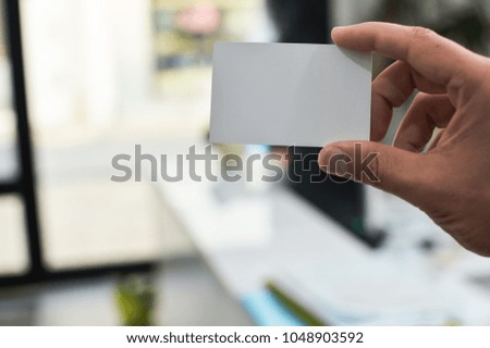 Close up on hand of a person holding showing white business card over blurry office background