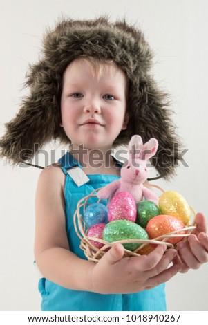 Little blond kid boy coloring eggs for Easter holiday in domestic room, indoors. Child holding basket with painted eggs. Child having fun and celebrating feast with easter toy bynny