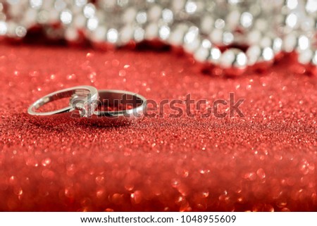 Two wedding rings on red glitter background