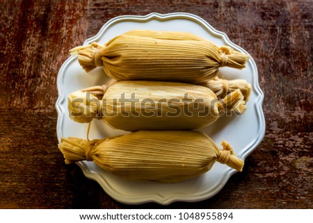 Unwrapped stacked Mexican tamales in white plate on grunge wooden table viewed from above - ethnic Food concept Royalty-Free Stock Photo #1048955894