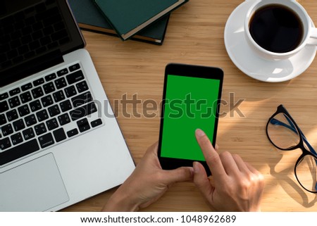 Top view of smartphone green screen display with hand, laptop, coffee cup and glasses.