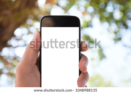 Hand holding smartphone against tree and sky on background
