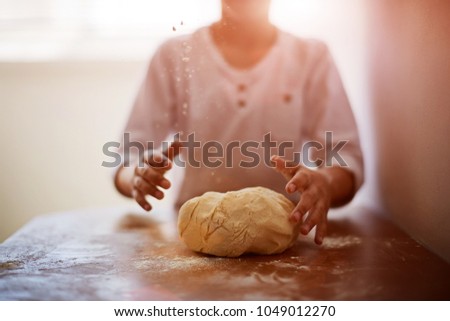 The little Boy in the kitchen himself in a white t-shirt hard kneads the dough