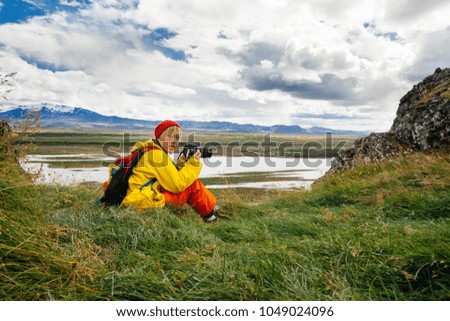 Happy young woman with photo camera  in bright clothes traveling Iceland, enjouing nature
