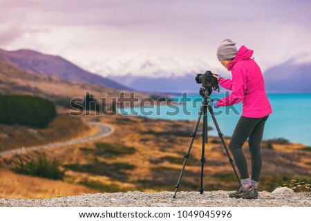 Travel photographer woman shooting nature photography mountain landscape at Peter's lookout, New Zealand. Girl tourist on adventure holiday with photo equipment, slr camera on tripod at dusk.