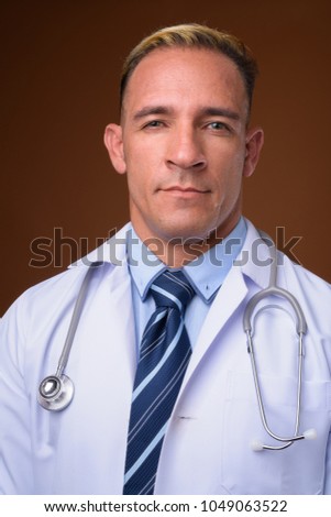 Studio shot of man doctor with dyed blond hair against brown background