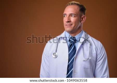 Studio shot of man doctor with dyed blond hair against brown background
