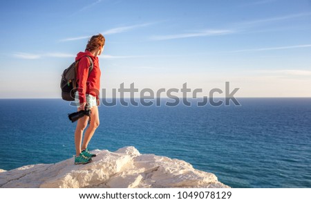 beautiful young woman traveler with a camera stands on a rock and looks at the horizon, freedom, summer travel, profession, freelancer, journalist, blogger, professional photographer