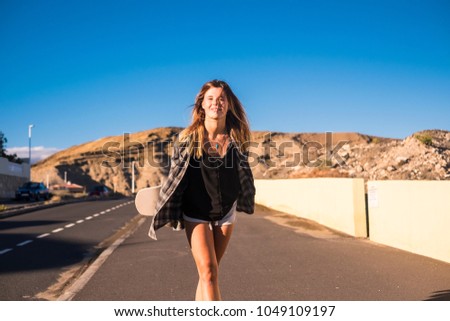 happiness concept for beautiful blonde caucasian young girl walking down the street with her skateboard. mountains on the background and blue clear sky
