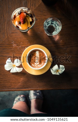 Flat white coffee with a dessert on a yellow plate from above. Wooden table at the minimalist hipster coffee shop. Latte art concept. 
