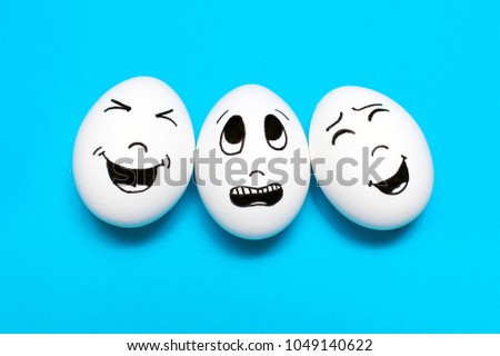 Three eggs with drawn cartoon faces on blue background. Friends concept