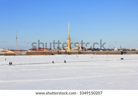 St. Petersburg City Winter Scene with Peter and Paul Fortress Architecture and People Walking on Frozen Snowy Neva River Surface in Russia. Cityscape Outdoor View of Downtown Saint Petersburg.