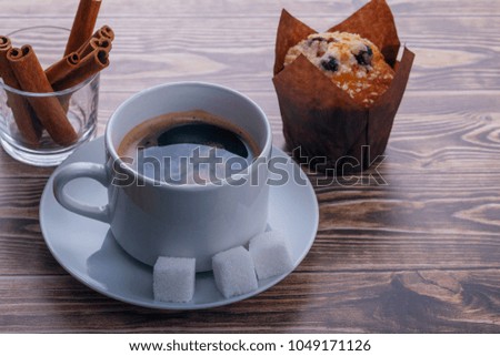 Coffee Cup with sugar cubes, muffin and cinnamon sticks closeup on wooden background