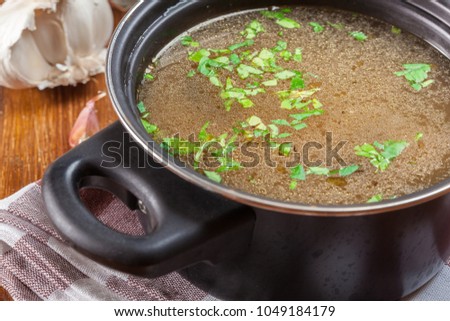 Tasty meat broth in a dark cooking dish on a wooden table