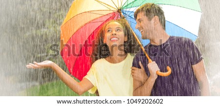 Multicultural young couple under rainbow umbrella during rainy stroll in the park