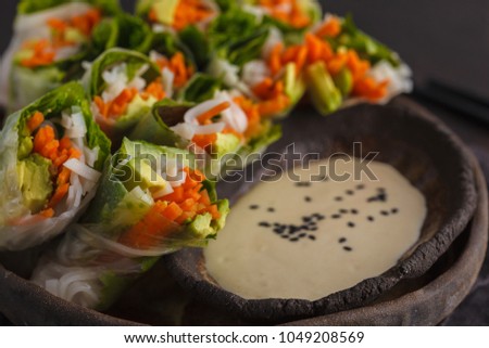 Fresh handmade vegan asian spring rolls with rice noodles, avocado, carrots and tahini dressing on black dish