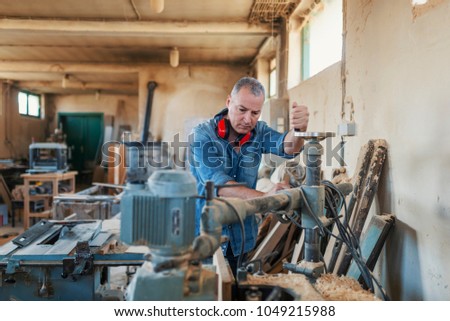Engineer in workshop. Carpenter is standing on electric cutter with ear protection. Carpentry workshop routine. Craftsman in uniform working at carpentry
