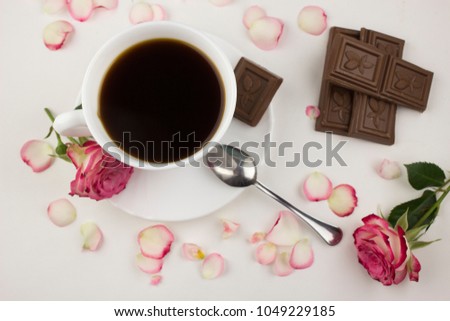 A cup of coffee, red roses on a white background and chocolate