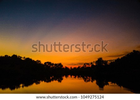 silhouette picture of river ,forest and hill after the sun setting in the evening time